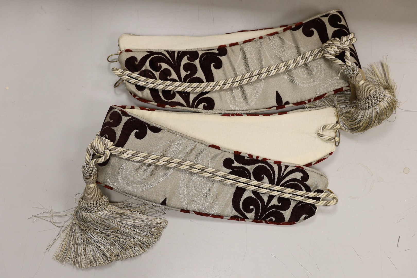 A large pair of silver brocaded curtains, with a woven paisley tear drop motif and large all over plum cut velvet Fleur-de-lis motifs, together with matching corded and tasselled tie backs.